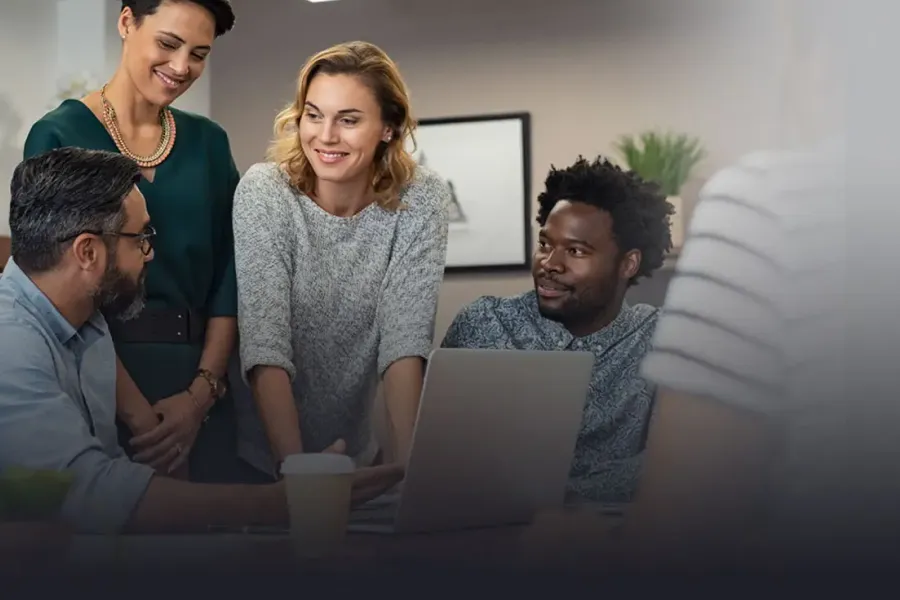 Four colleagues smile at each other while working in an office setting.