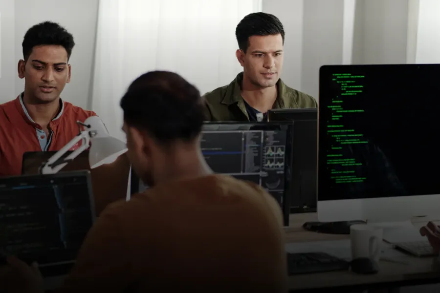 Three cyber security professionals smile working on technical projects on computers.
