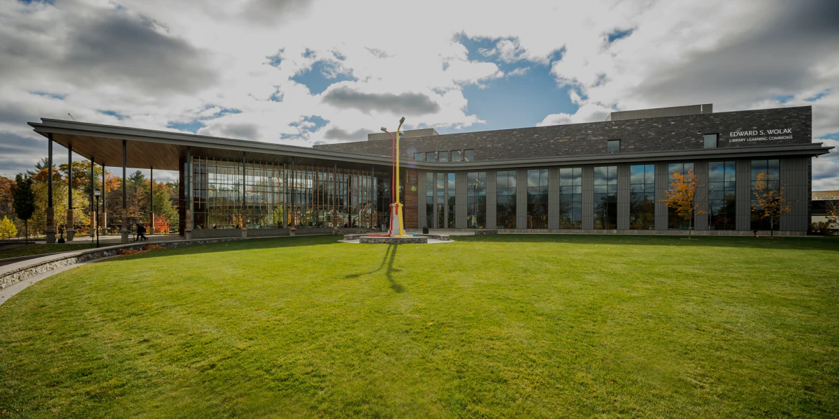 A modern, glass-covered building on SNHU’s campus in New Hampshire in front of a large green lawn.