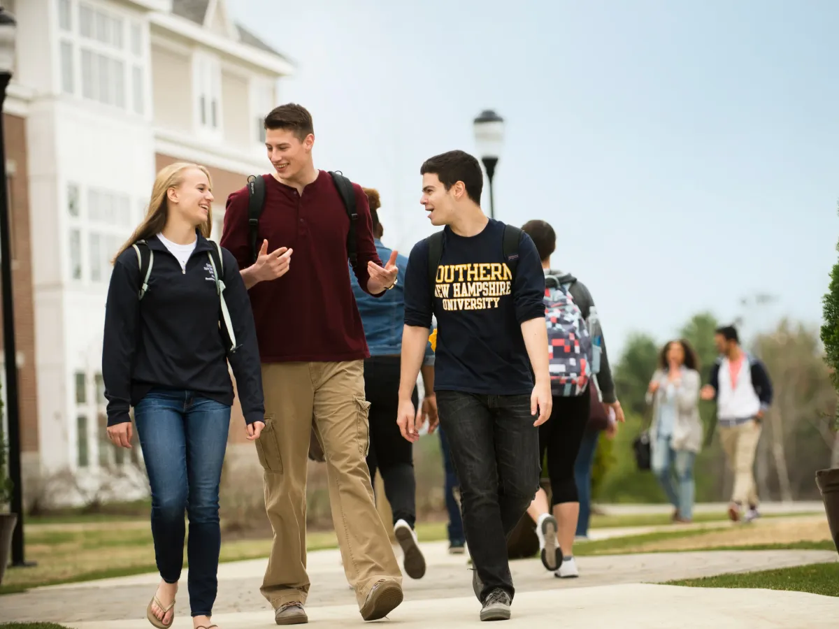 Three young students walk through SNHU’s campus talking and smiling.