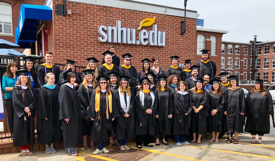 Photograph of a group of graduates in their gowns in front of the SNHU campus