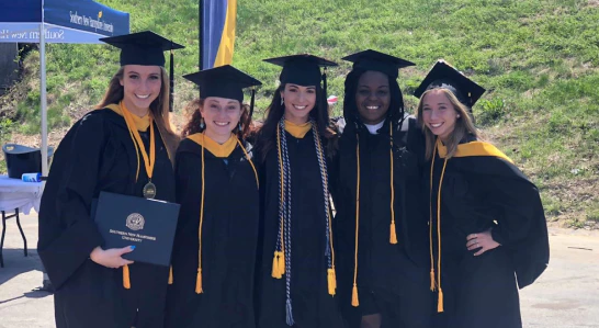 Photograph of five smiling interracial female students dressed in graduation gowns