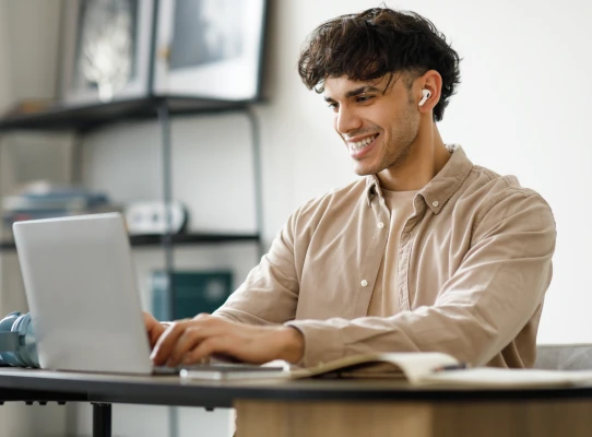 Person wearing headphones looking at their laptop while smiling.